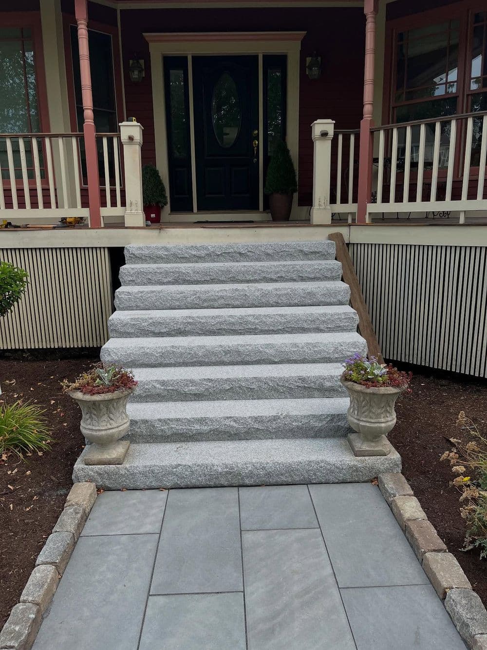 Granite steps leading to a charming porch with potted plants and a welcoming front door.
