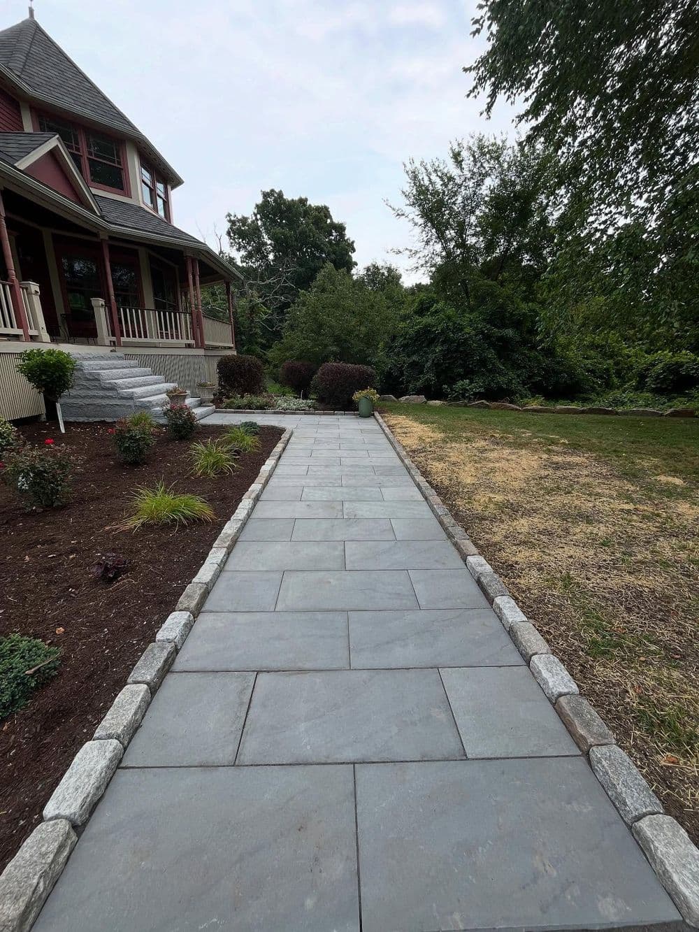 Walkway made of slate pavers leading to a house with landscaped garden and trees.