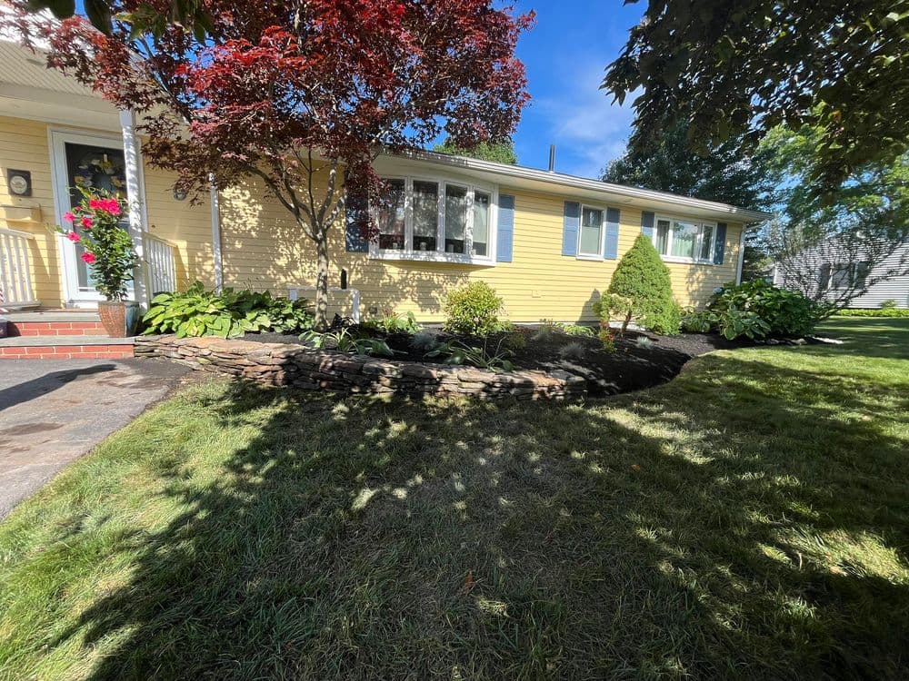 Yellow residential home with landscaped garden, stone pathway, and vibrant trees.