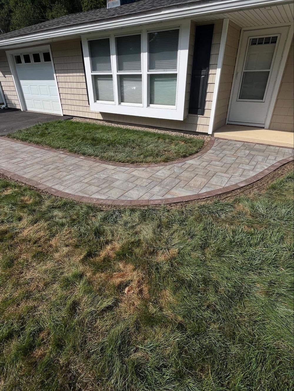 Paved walkway leading to a house, featuring a manicured lawn and shrubs.
